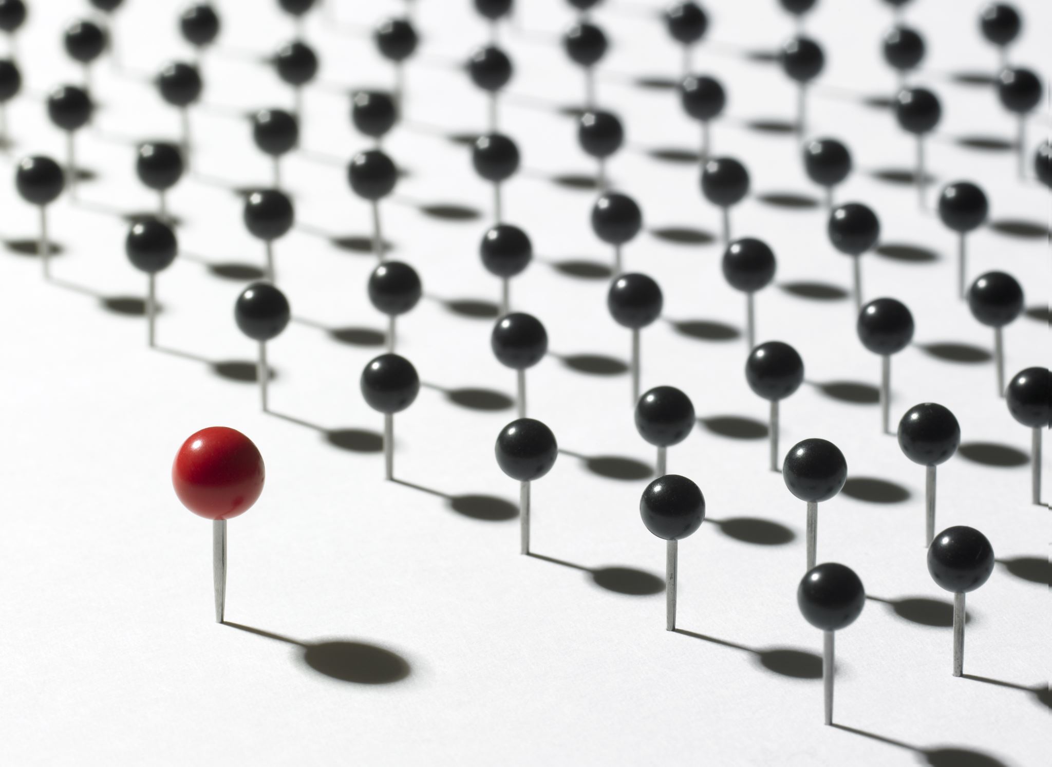 One big red thumbtack in front of many smaller black thumbtacks